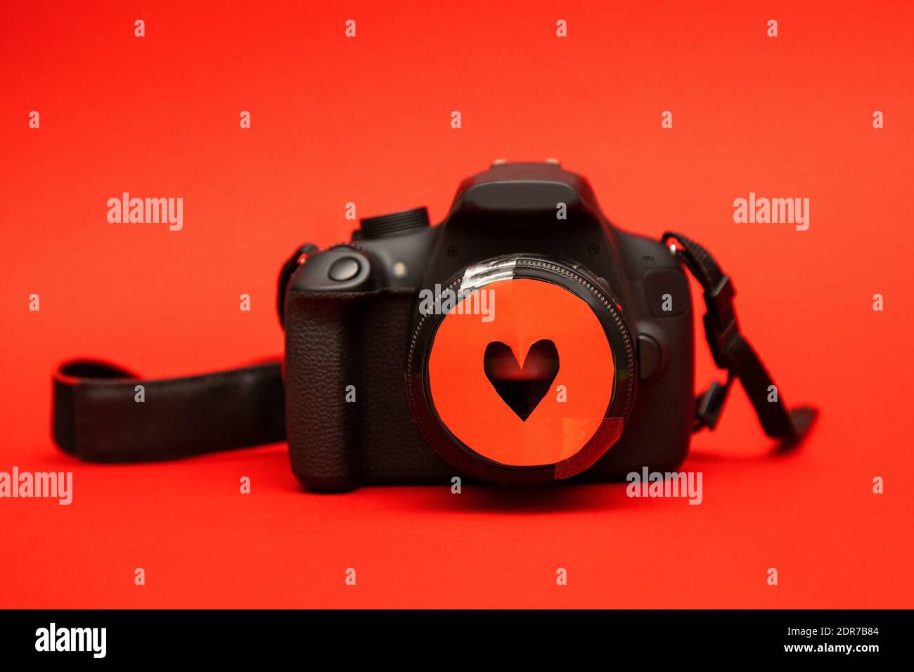The concept of love through photography. Black camera with red carved heart on piece of paper attached to lens. Creative idea. Close-up photo Stock Photo