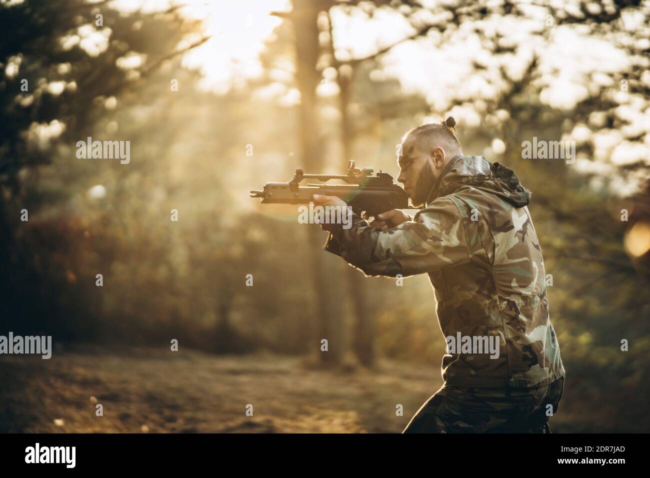 Side View Of Army Soldier Aiming Gun In Forest Stock Photo