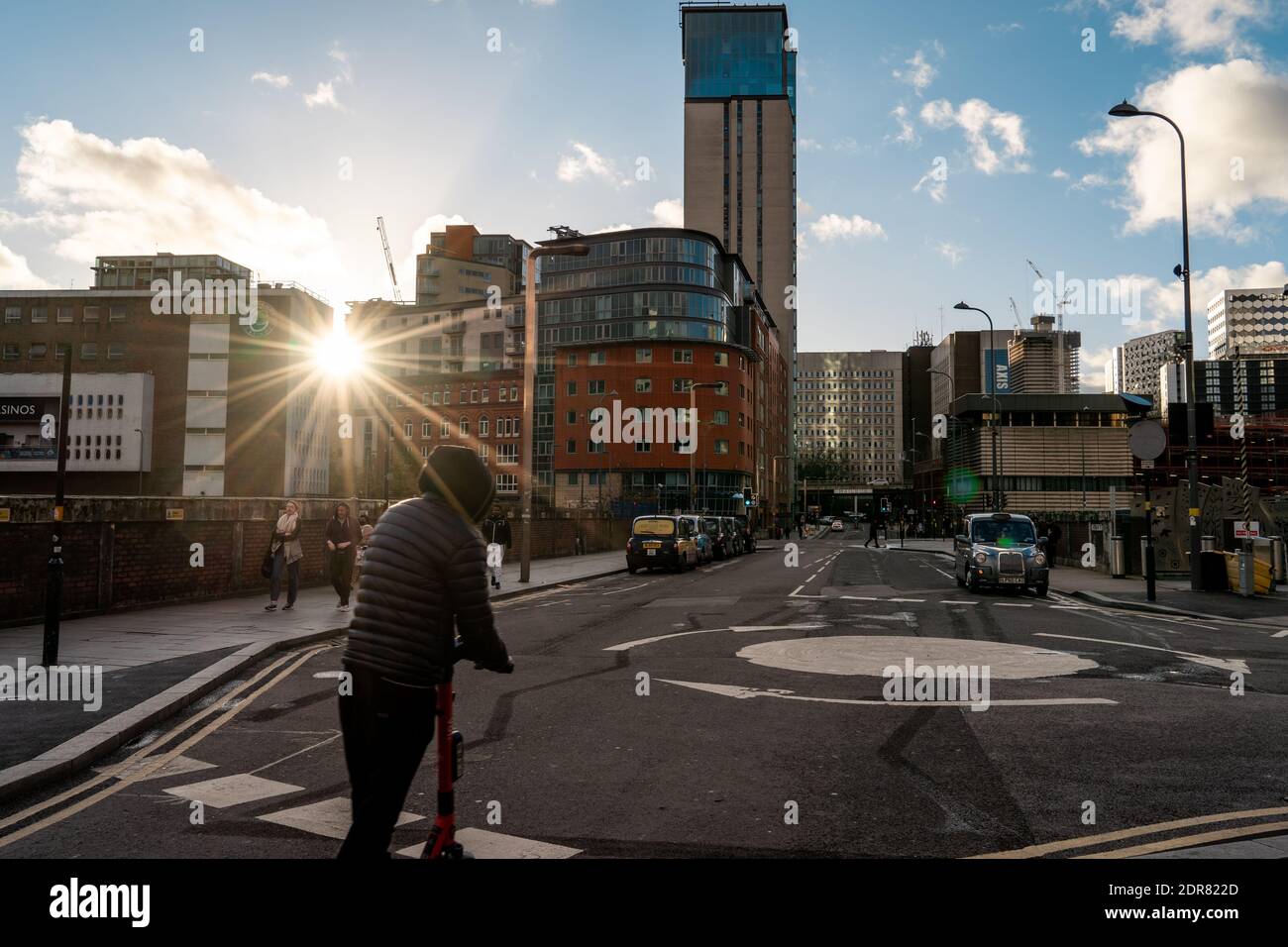 Birmingham cityscape with setting sun over buildings, pedestrians walking and man on electric scooter Stock Photo