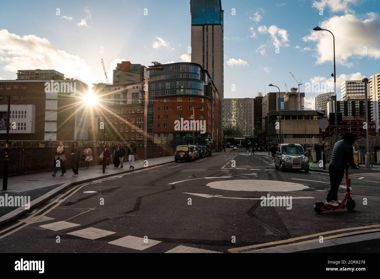 Birmingham cityscape with setting sun over buildings, pedestrians walking and man on electric scooter Stock Photo