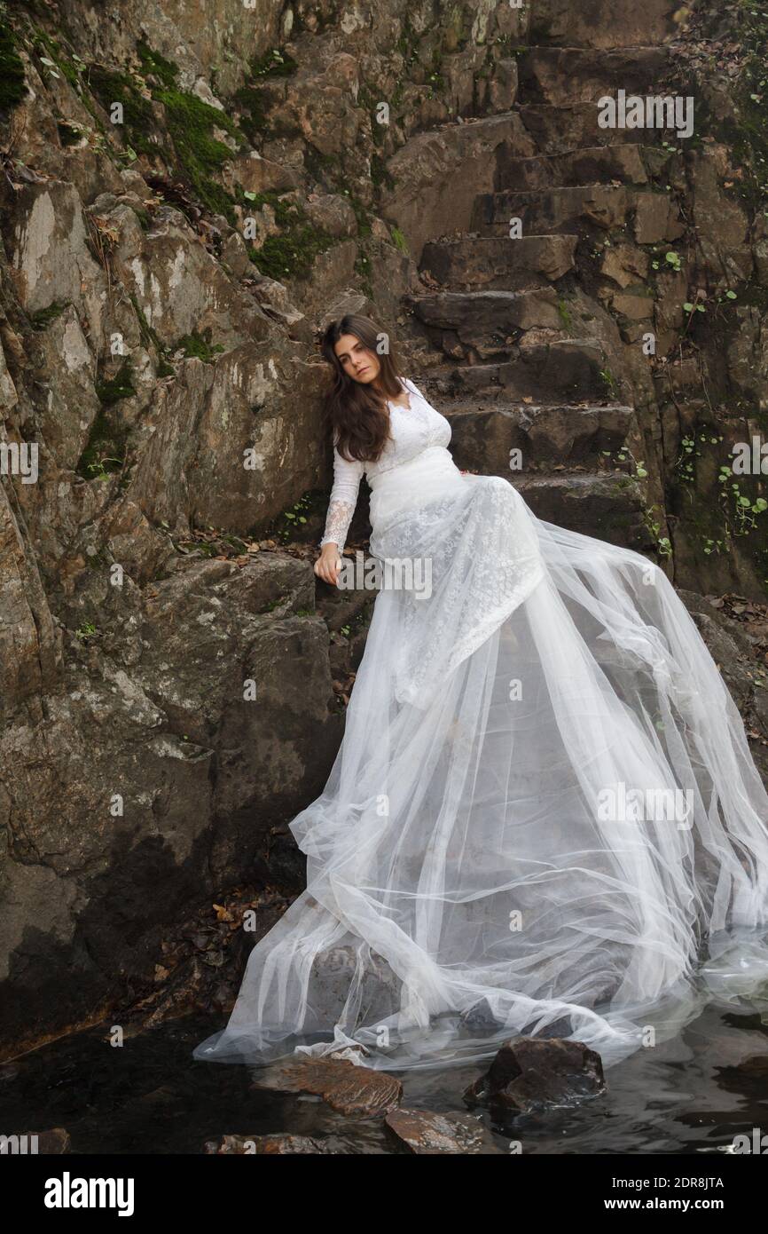 Bride Wearing White Wedding Dress Sitting On Rocks Stock Photo - Alamy
