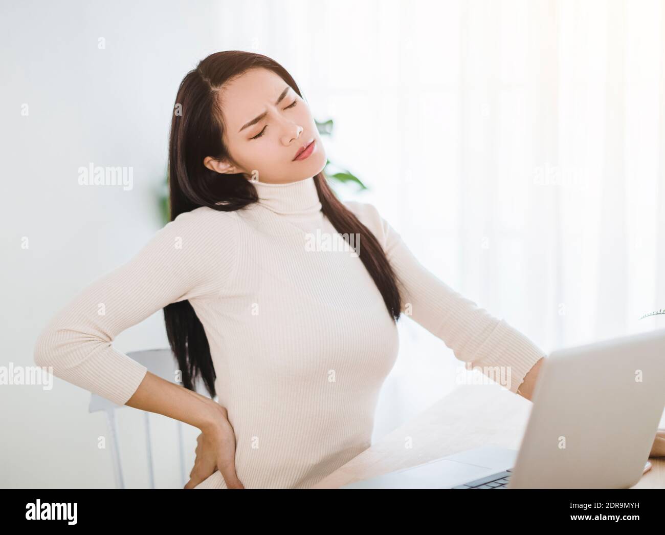 young woman suffering from backache after working on laptop Stock Photo