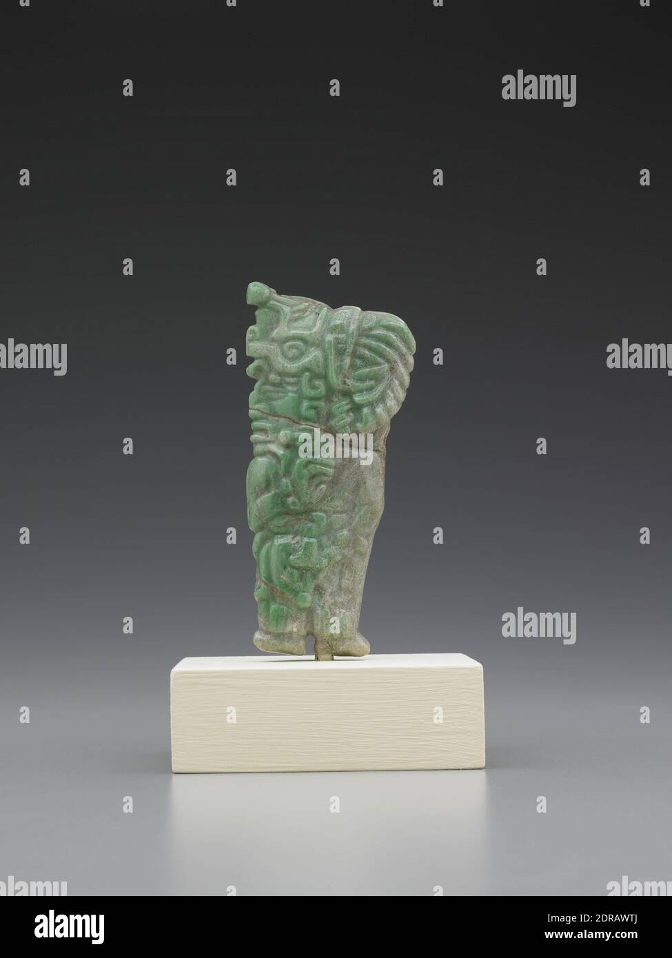 Pendant in the  Shape of a Ruler or Lord, A..D. 200–600, Jadeite, 9.98 × 4.17 × 1.73 cm (3 15/16 × 1 5/8 × 11/16 in.), This pendant in the shape of a standing male figure probably once belonged to a Maya noble.  The craggy nose and specific details of the headdress may indicate that the pendant was intended to be a portrait of a particular individual, possibly the owner himself.  The beaded tassel at the top of the headdress is that of the Jester God and is a common attribute of kings and nobles. Stock Photo