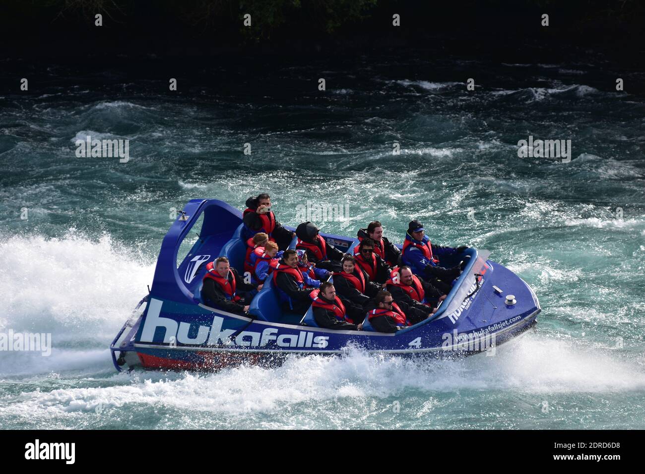 Huka Falls tourist jet boat pacing through rough waters of river. Stock Photo
