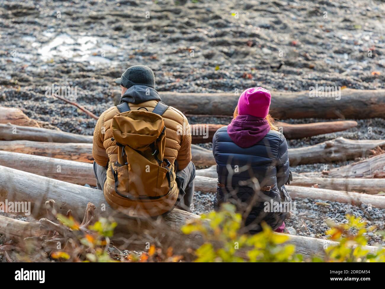 Young couple sitting on the shore by the sea enjoying the sunset on a cold winter evening West Vancouver. Travel photo, street view, selective focus. Stock Photo