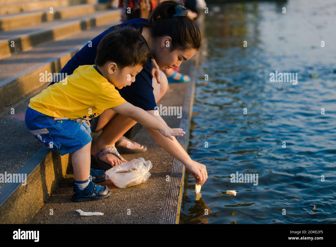 Side View Of Mother And Son Throwing Bread In Lake Stock Photo Alamy