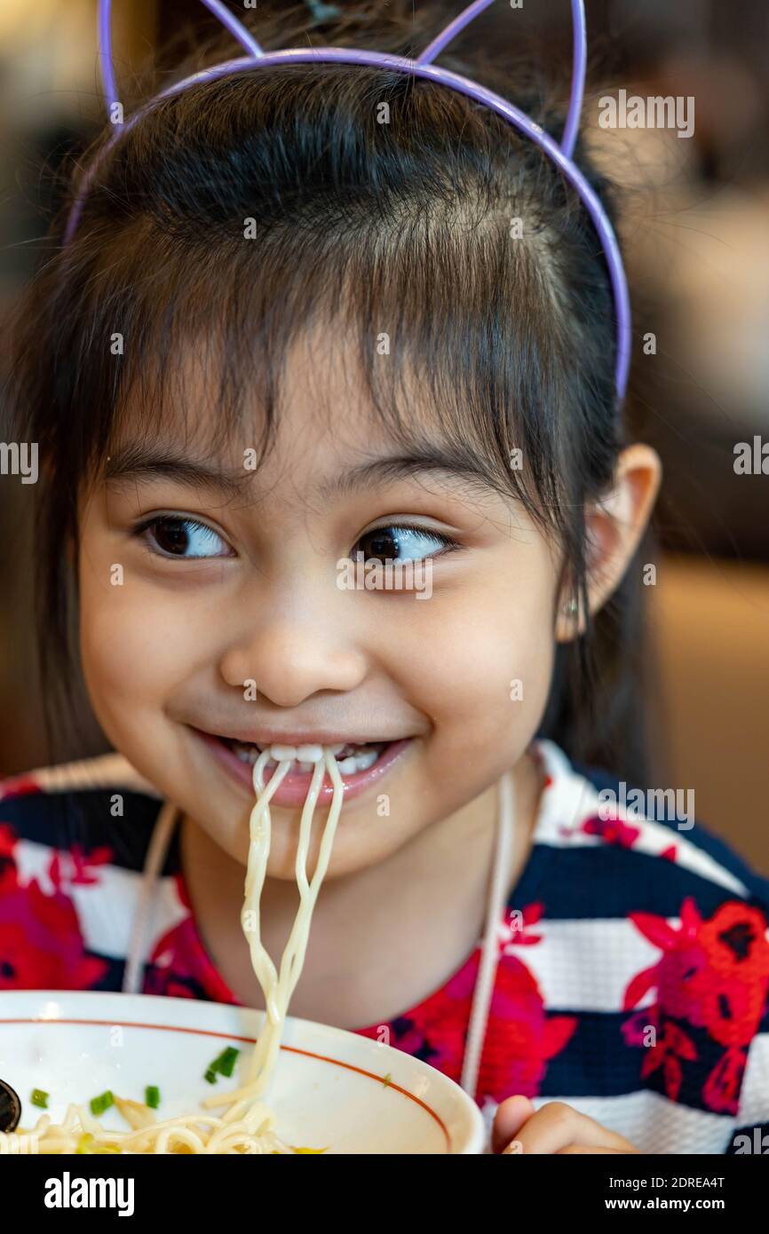 Female asian child while eating noodles. Child eating ramen noodles