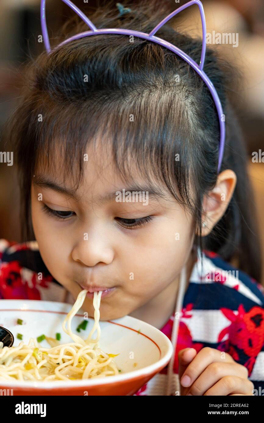 Female asian child while eating noodles. Child eating ramen noodles