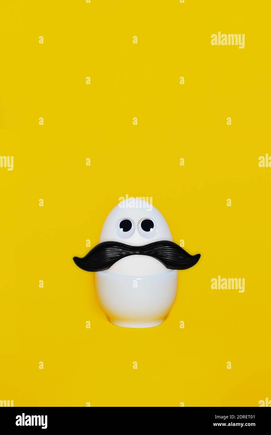 Easter funny eggs man with black mustache. Creative minimal easter egg concept. White egg on yellow background. Copy space. Stock Photo