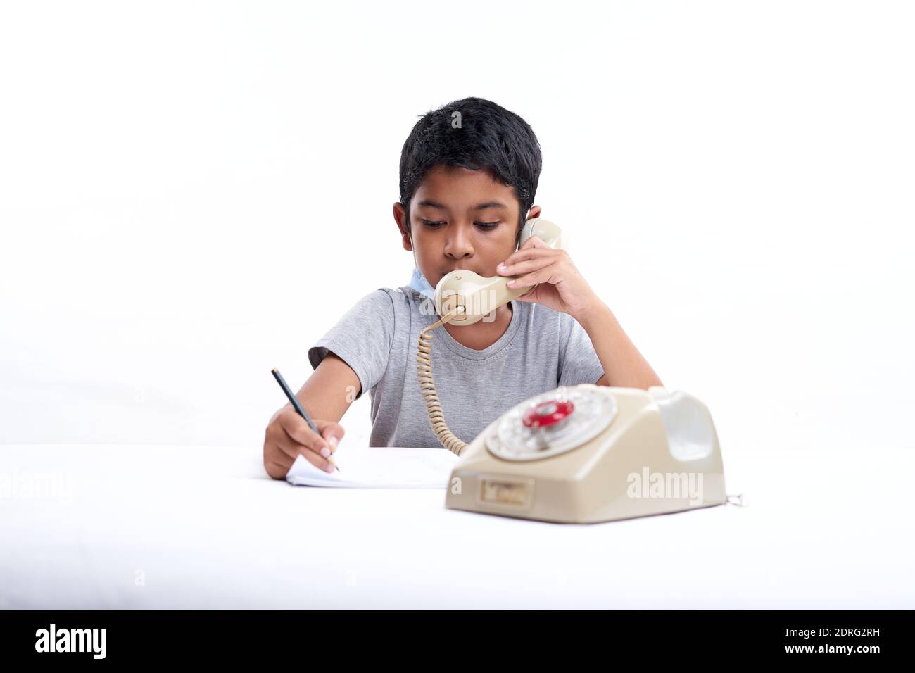 Young boy Talking on vintage telephone and making notes during online class at home Stock Photo