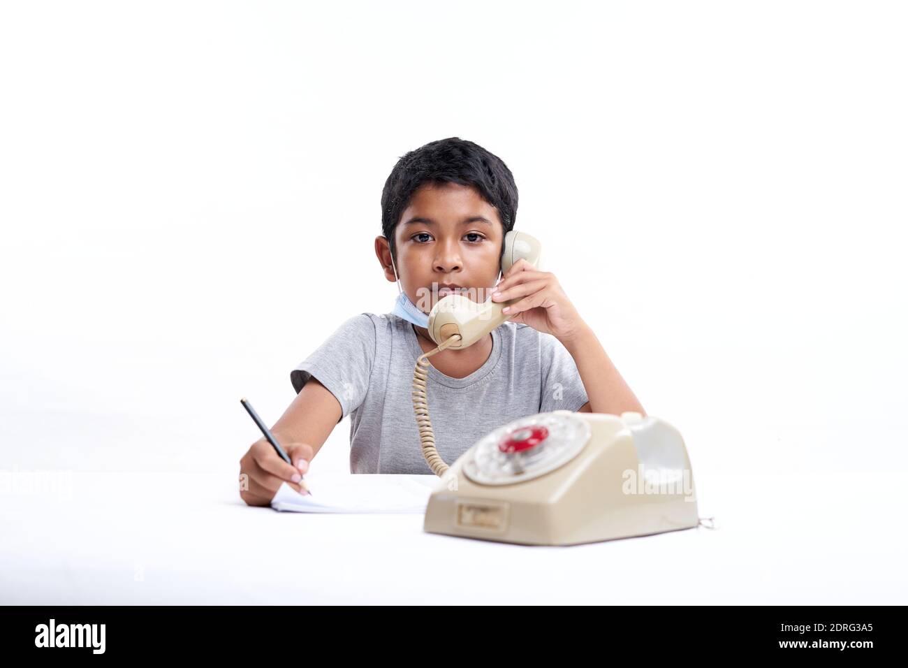 Young boy Talking on vintage telephone and making notes during online class at home Stock Photo