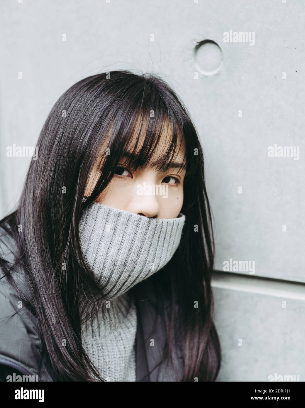 Closeup Portrait Of Young Woman Covering Mouth With Turtleneck Against