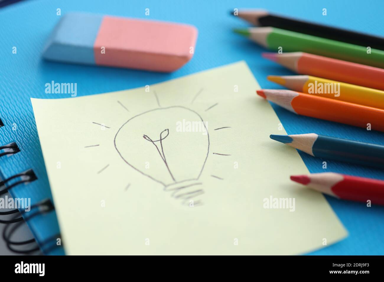 On white sheet of paper, light bulb is drawn next to colored pencils ...