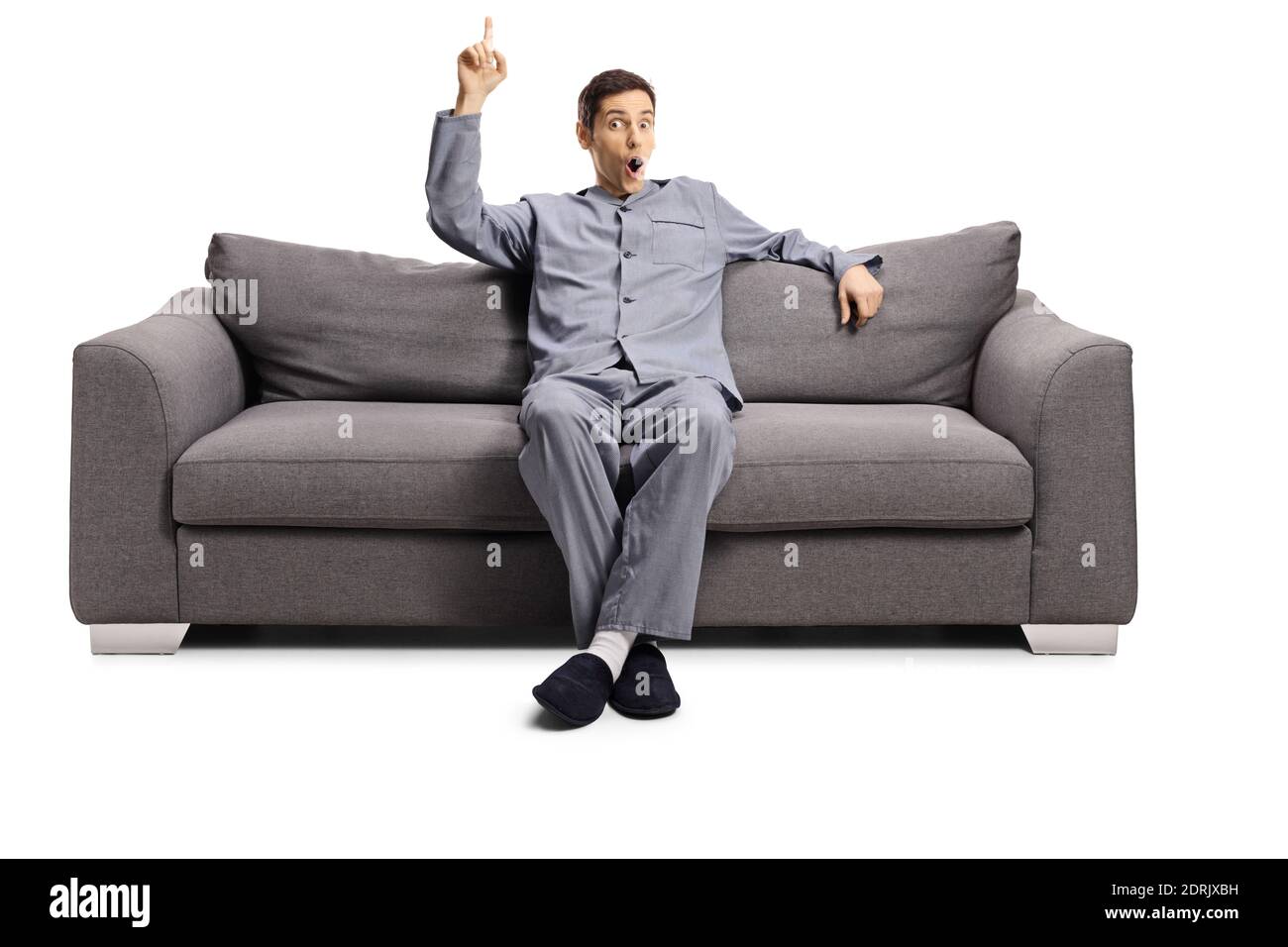 Young man in pajamas seated on a sofa pointing up isolated on white background Stock Photo