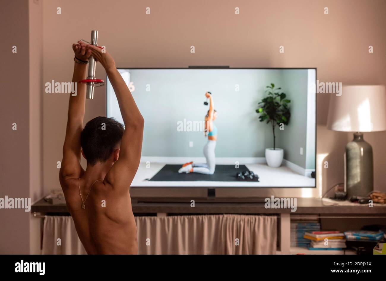 Workout in front of the TV: young man following a YouTube workout session during the lockdown due to the coronavirus / Covid-19 outbreak. Stock Photo