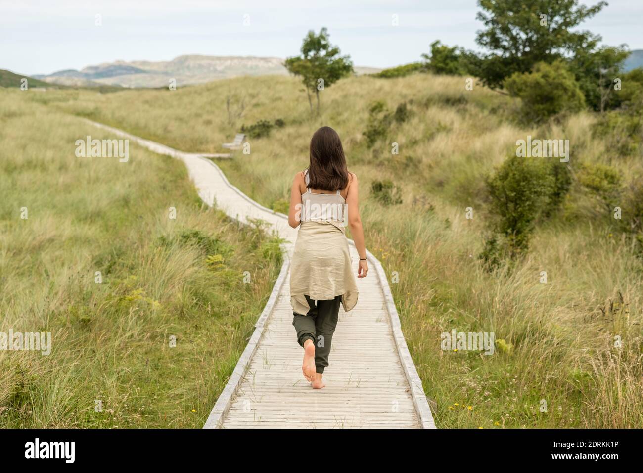 A young woman walks barefoot on a wooden path in Ards Forest Park, a few kilometers from Dunfanaghy in Ireland Stock Photo