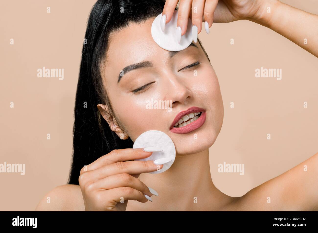 Young asian woman with eyes closed, enjoying cleaning of face, using