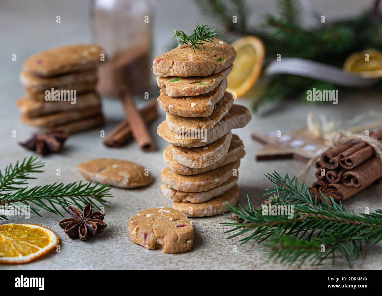Stacked spicy butter cookies with candied fruits, cinnamon sticks and anise. Festive Christmas or New Year background with fir branches and dried oran Stock Photo