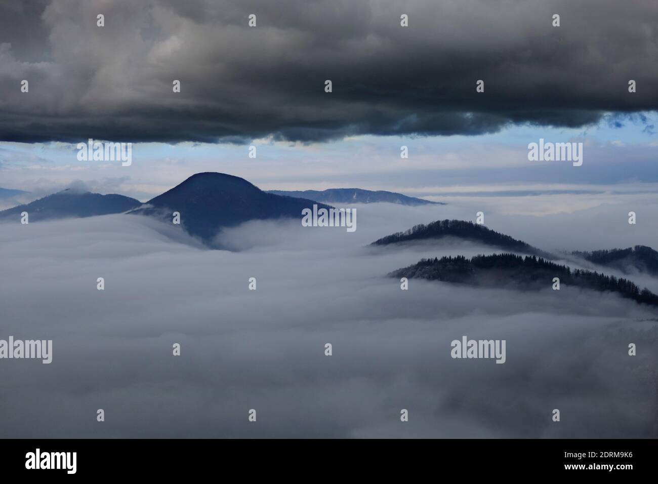 Mountain peaks visible above dense fog with heavy clouds above. Stock Photo