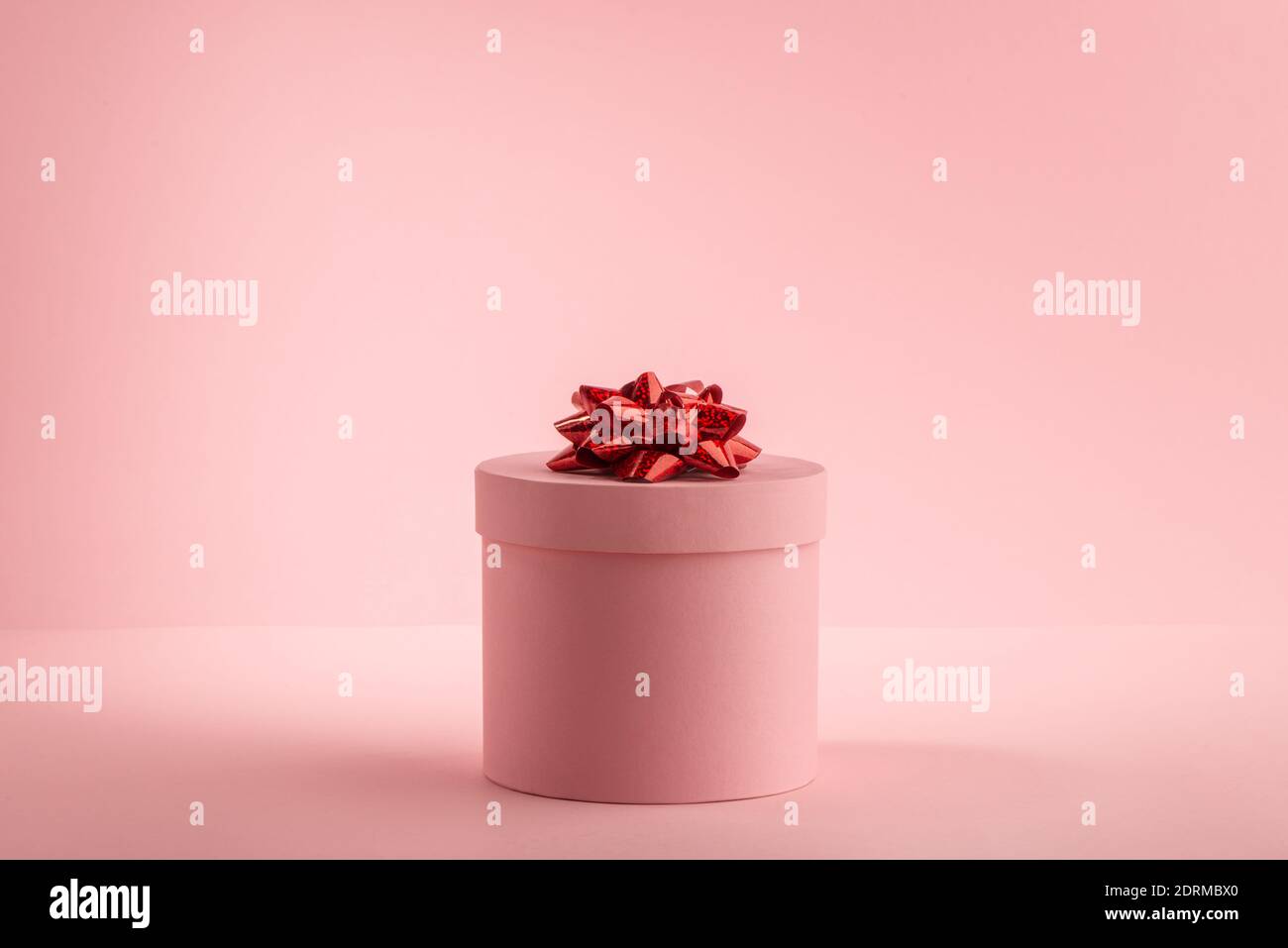 Round gift box with red bow on pink background Stock Photo - Alamy