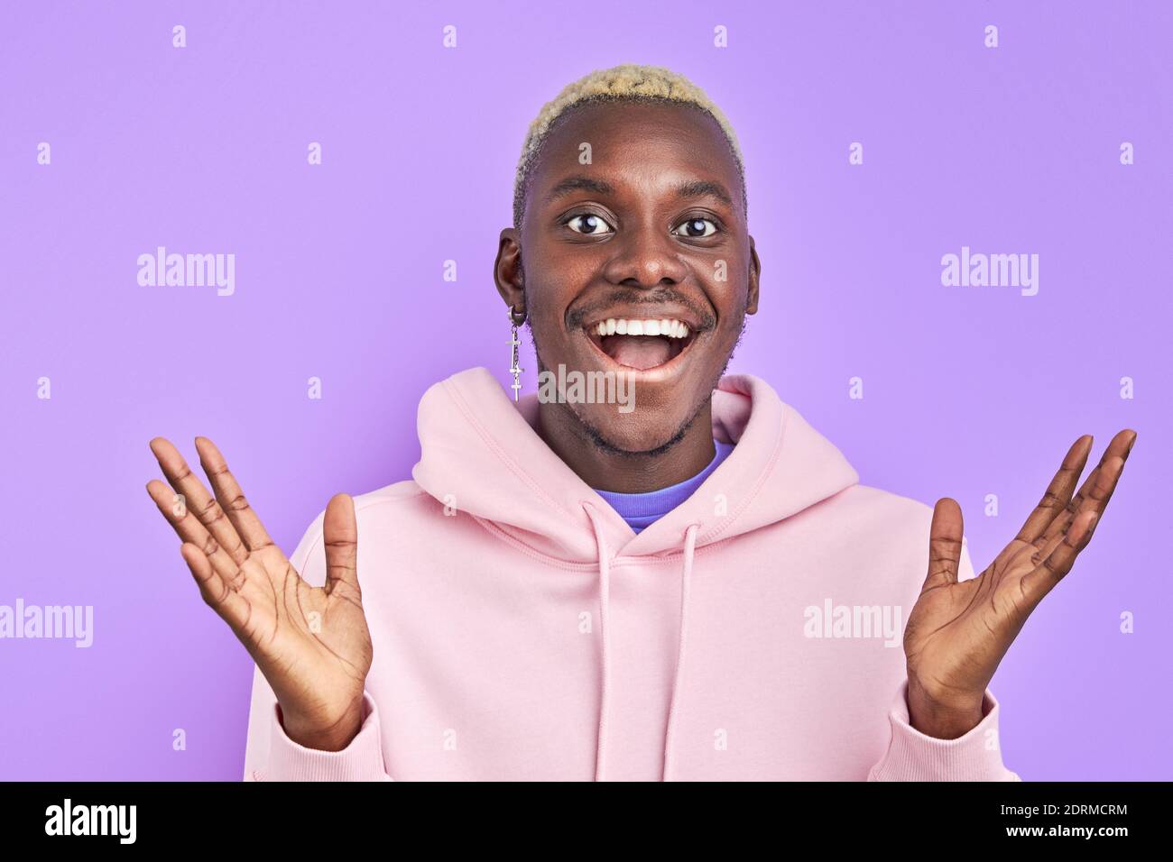 black man is gesturing with hands after getting news, he is surprised, stand with opened mouth. isolated on purple background. portrait in studio Stock Photo