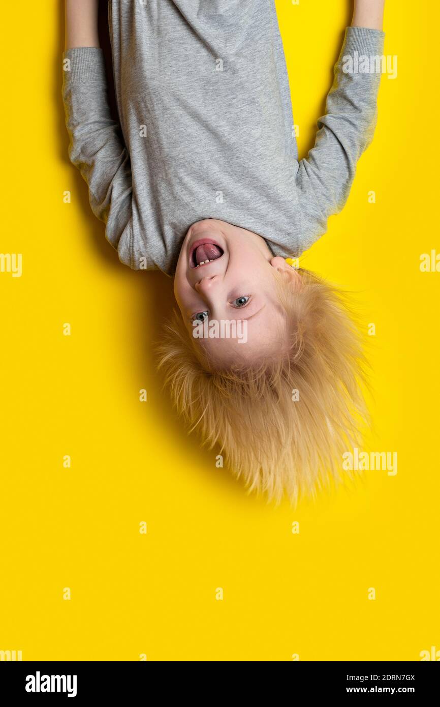 Frightened child hanging upside down. Portrait of boy with long white hair  on yellow background. Vertical frame Stock Photo - Alamy