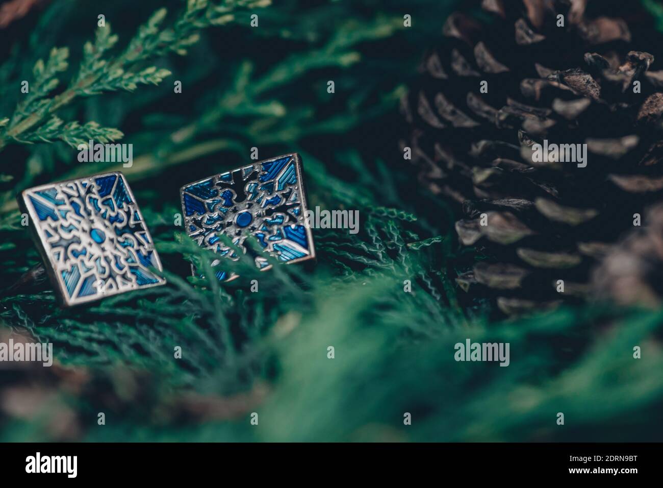 Thame,UK - 25 Nov 2020: Blue cufflinks in silver on evergreen and pinecones background, snowflake pattern on each cufflink, christmas mens jewellery Stock Photo