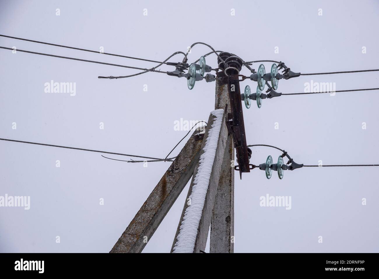 Power line sprinkled with snow against the background of a cloudy sky on a winter day. Stock Photo