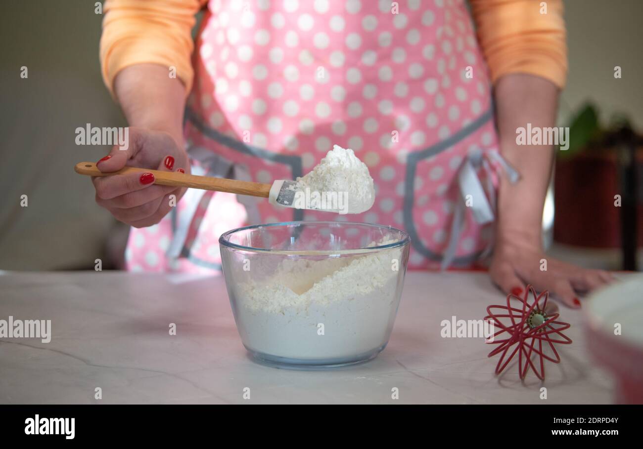 woman mixing flour in a glass bowl with a pink apron at home Stock Photo