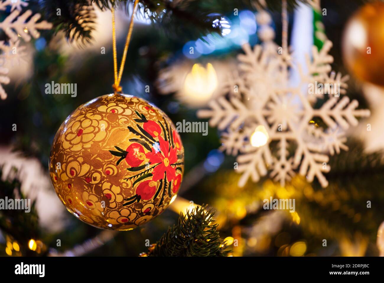 Golden christmas bauble hanging on a Christmas tree, with lights and decorations in the background. Stock Photo