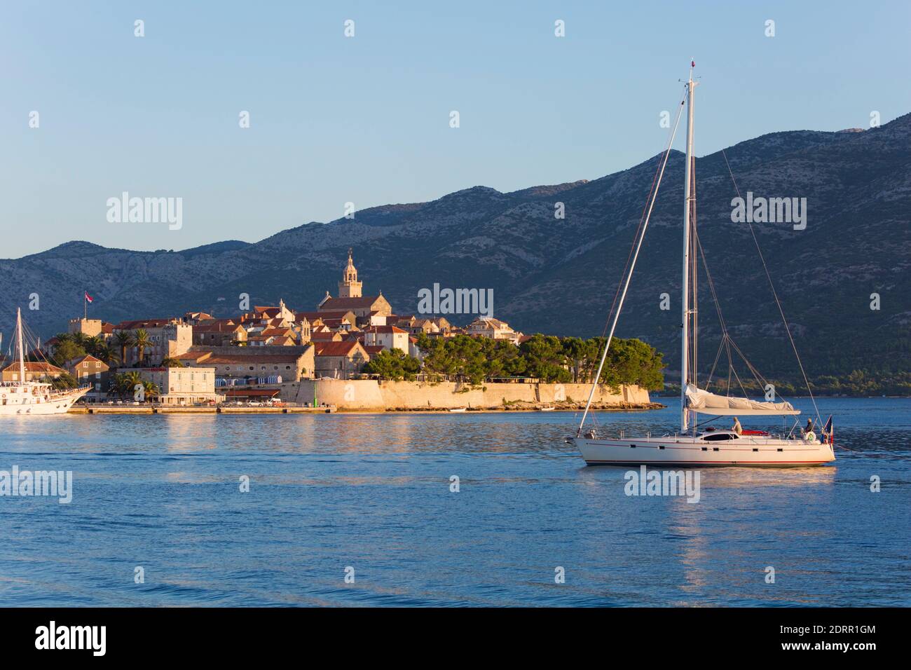 Korčula Town, Korčula, Dubrovnik-Neretva, Croatia. View across bay to the Old Town, sunrise, yacht sailing into harbour. Stock Photo
