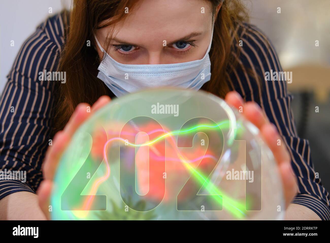 A gypsy woman wonders about the future of the coronavirus in 2021 on the ball of fate. Witch in a face mask over a crystal ball predicts the future of Stock Photo