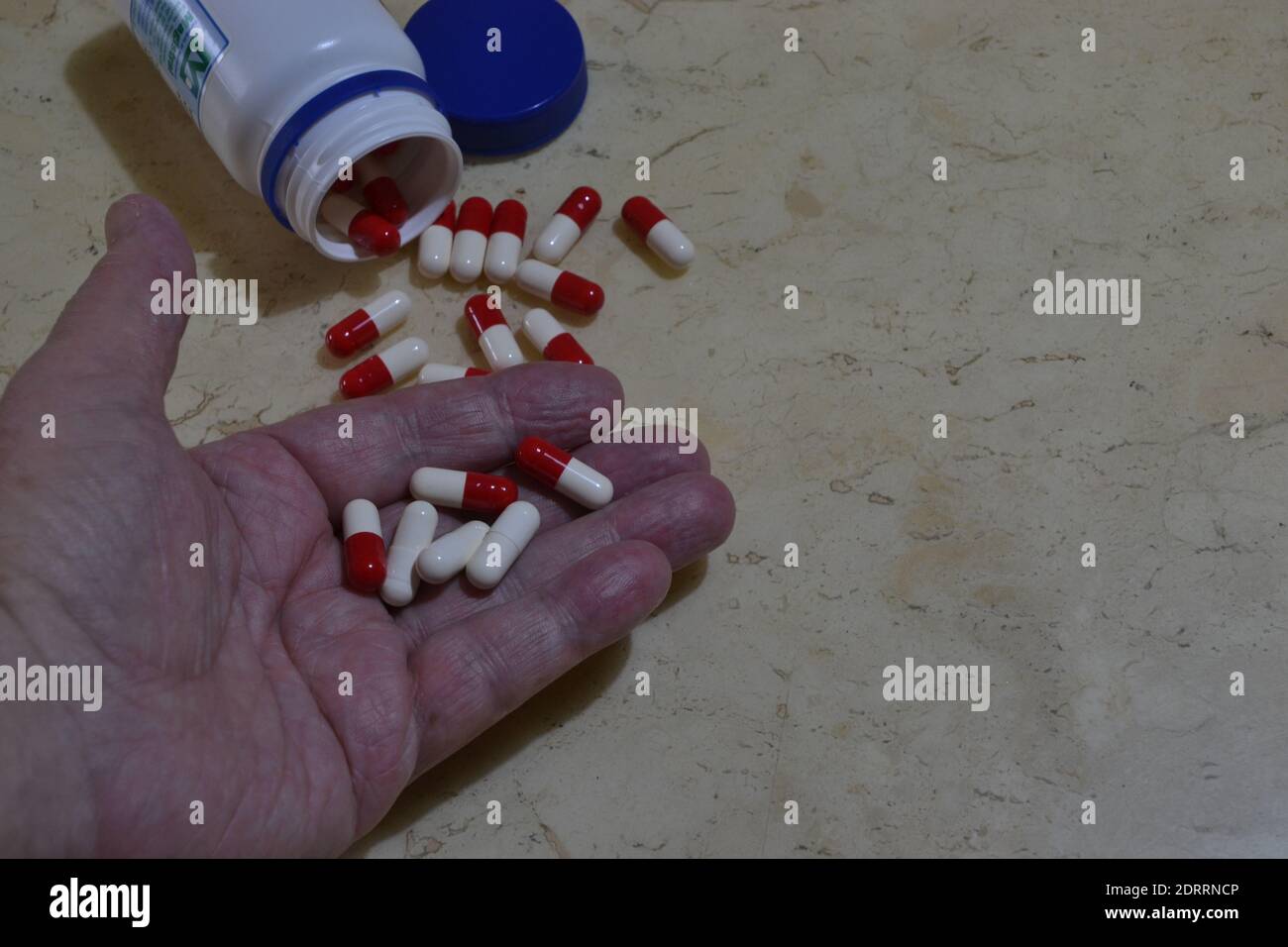 Elderly man with handful of pills to take for treatment, jar of red and white pills on marble background, Brazil, South America Stock Photo