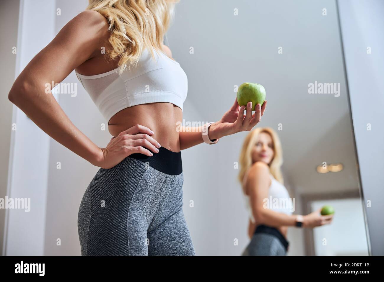 Sport woman in white bra standing in front go the mirror with fruit in cozy room Stock Photo