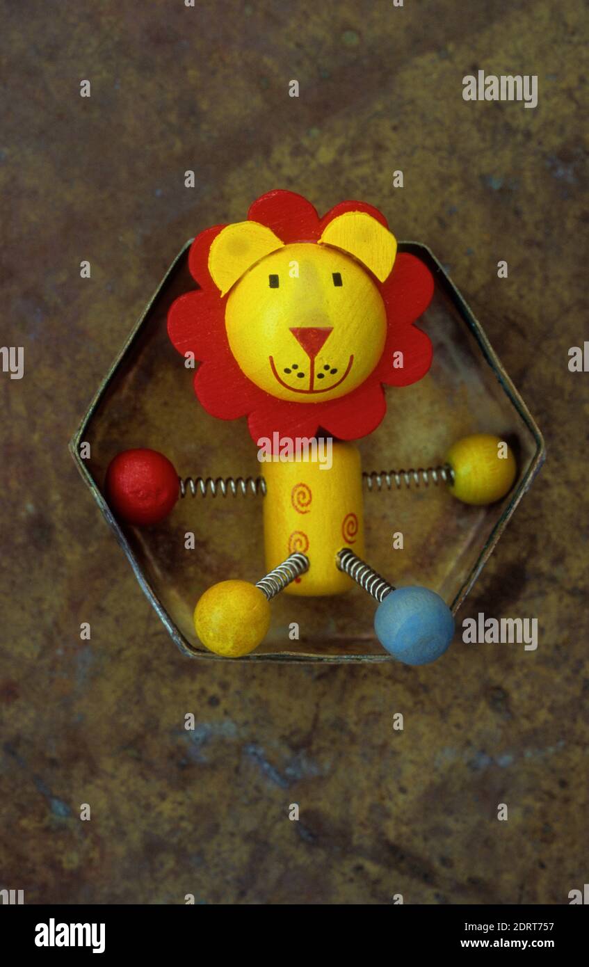 Wooden model of yellow and red lion with springy legs and friendly face lying in brass lid Stock Photo