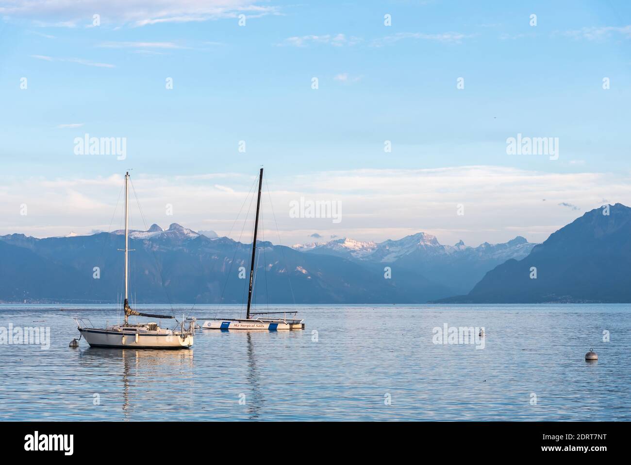 Alpine lake with the calm blue water with two boats moored surrounded by snowy peaks. Montreux in Geneve lake Stock Photo