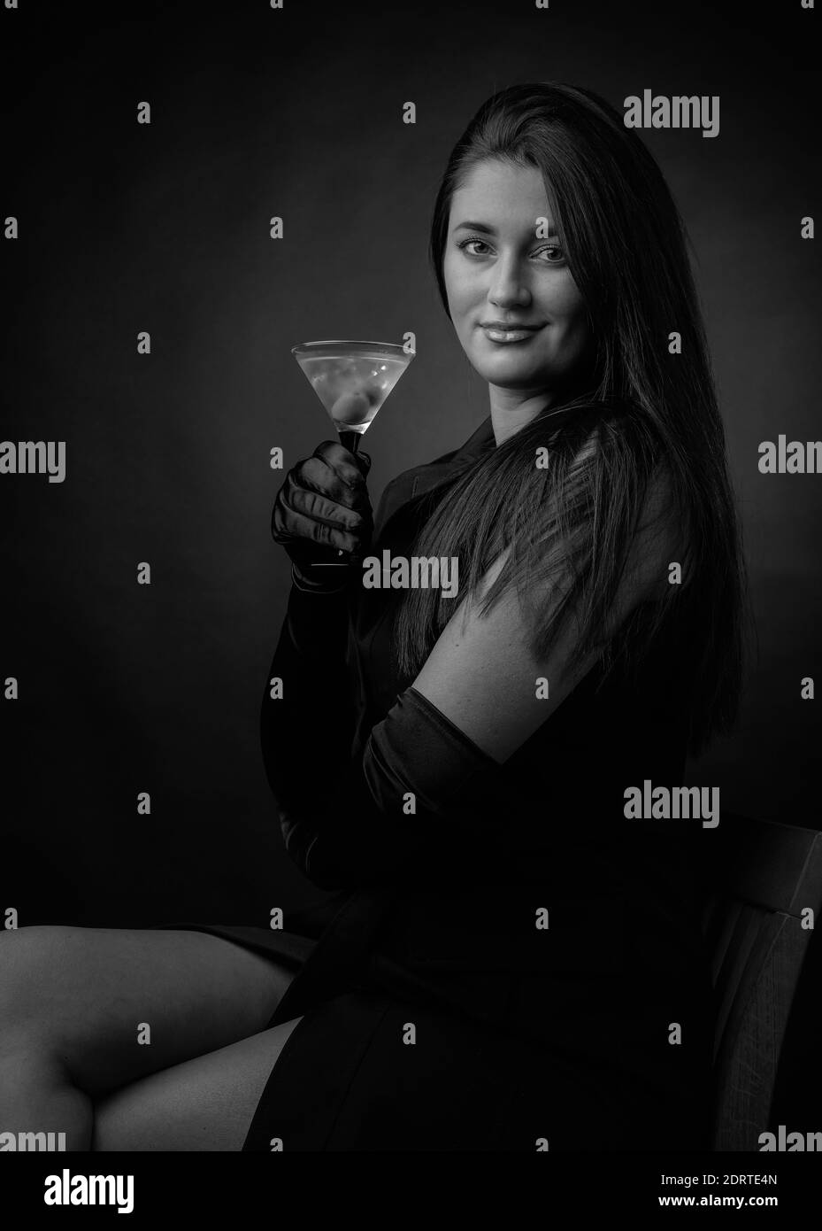 Attractive girl drinking dry martinis with green olives. Beautiful brunette in black holding glass with cold cocktail. Black and white. Stock Photo