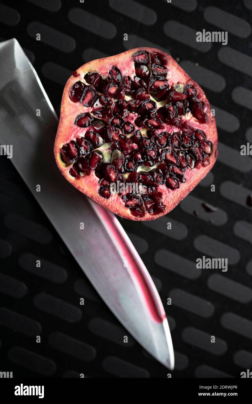 Sliced fresh pomegranate on a black background and a knife beside it Stock Photo