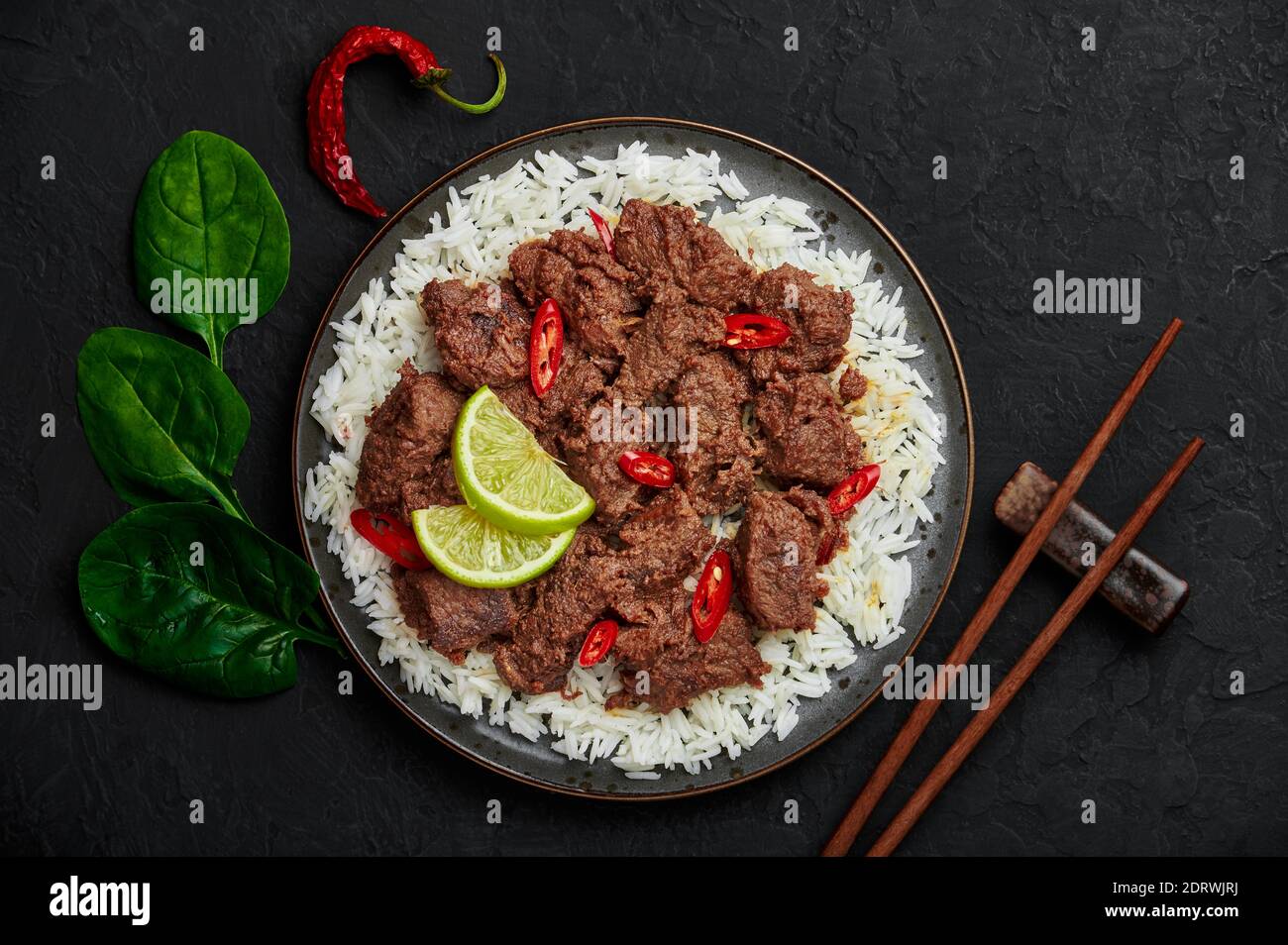 Beef Rendang on black plate at black slate table top. Indonesian padang cuisine meat dish. Asian