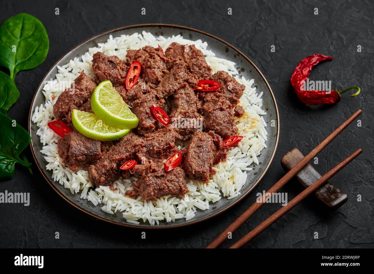Beef Rendang on black plate at black slate table top. Indonesian padang cuisine meat dish. Asian food. Stock Photo