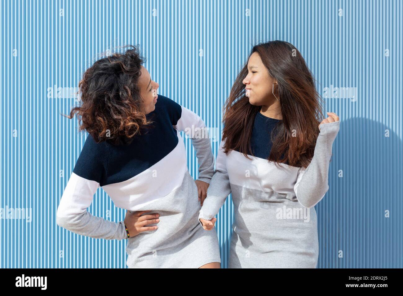 Two brunette girls in the same dress having fun on a blue background. Friendship concept. Stock Photo