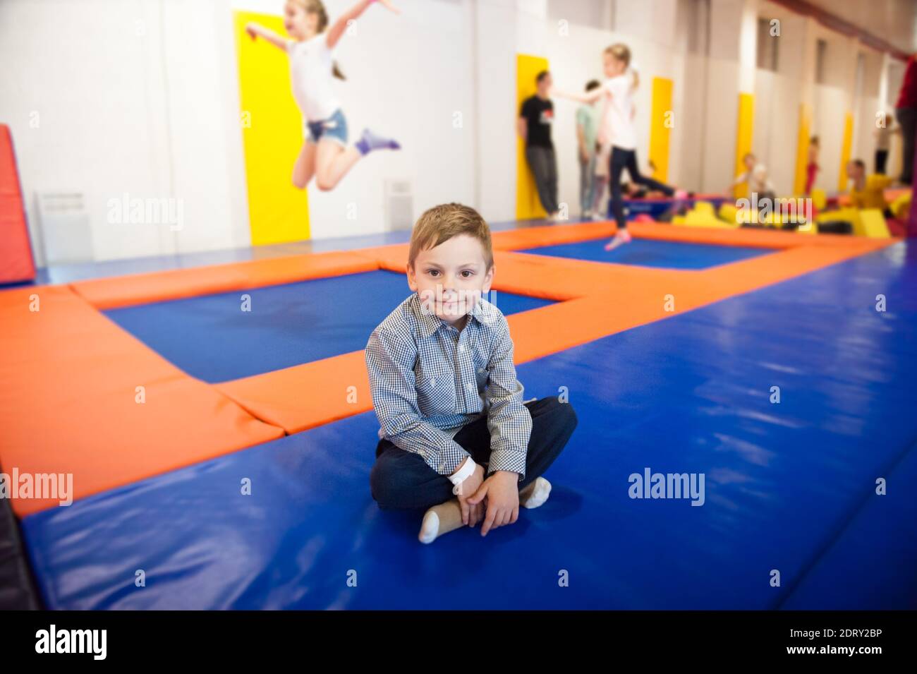happy smiling little boy sitting on trampoline among jumping kids ...