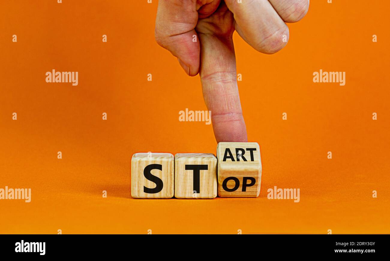 Stop or start symbol. Male hand flips a wooden cube and changes the word 'stop' to 'start'. Beautiful orange background, copy space. Business and stop Stock Photo