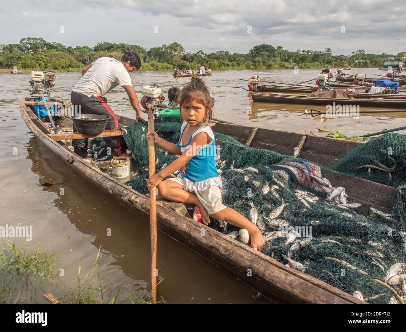 Amazon river, Peru- December 11, 2017: Small peruvian girl is  sitting on the wooden boat full of fishes. Stock Photo