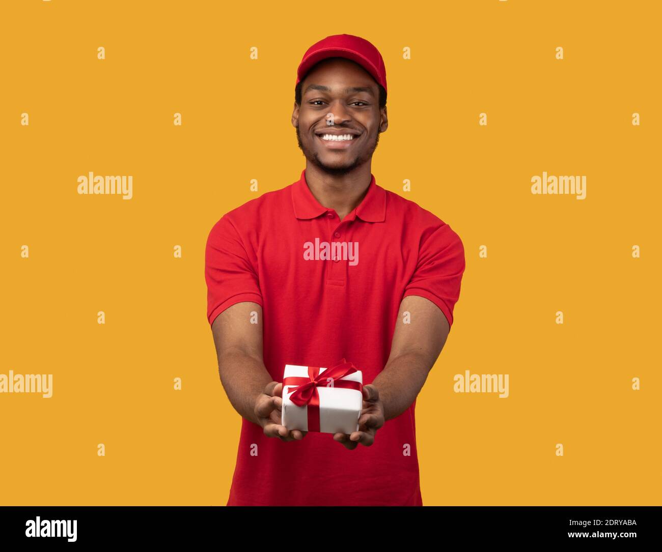 Black delivery man holding gift box giving it to camera Stock Photo