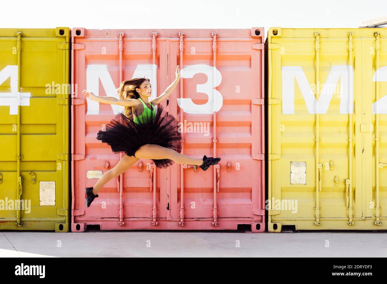 Dancer with tutu jumping in front of colorful industrial containers