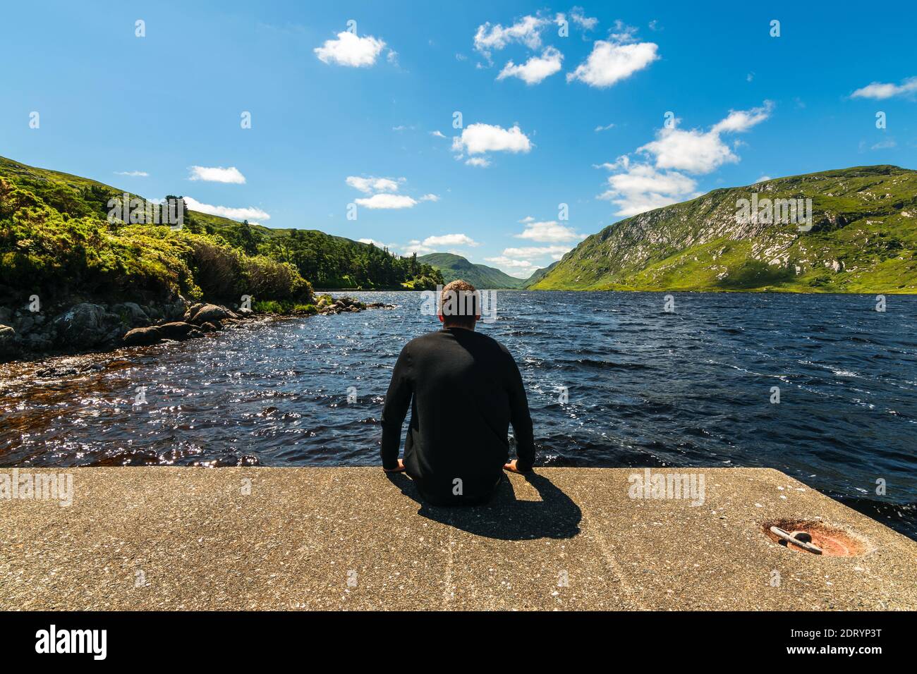 Young man enjoying view of Lough Veagh and rugged Derryveagh Mountains with blue sky in Glenveagh National Park north west of County Donegal, Ireland Stock Photo