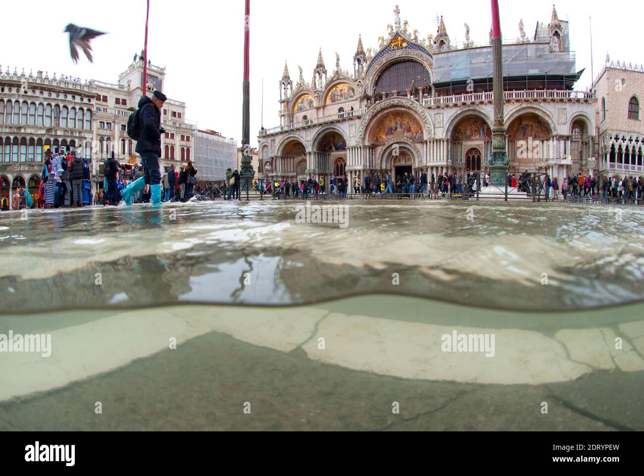 Underwater photo St. Mark's Square flooded by high tide with tourists walking by. Venice, Italy Stock Photo