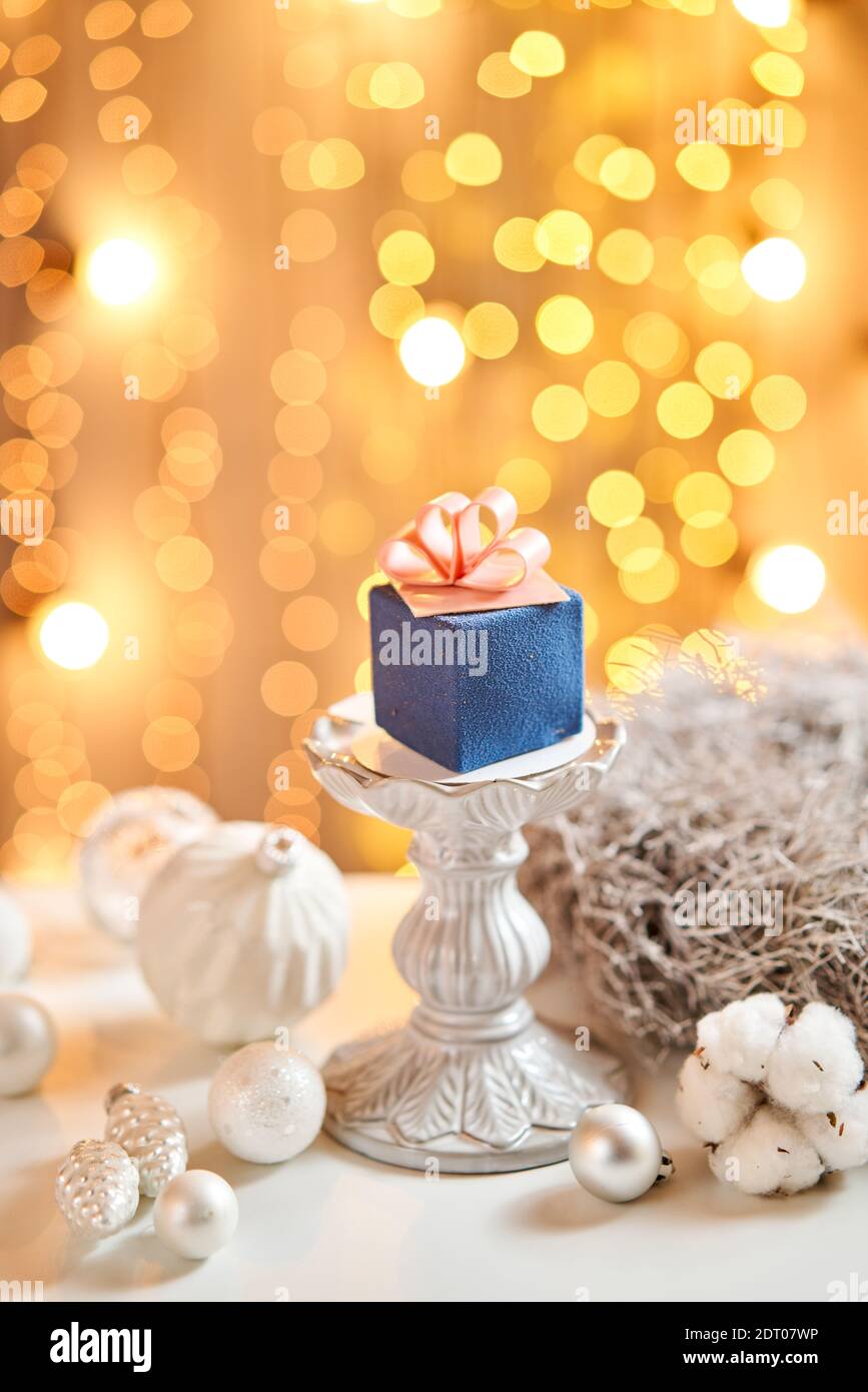 Mini mousse pastry dessert with blue velour. garland lamps bokeh background. In the form of gift box, ribbons of chocolate. Modern european cake Stock Photo