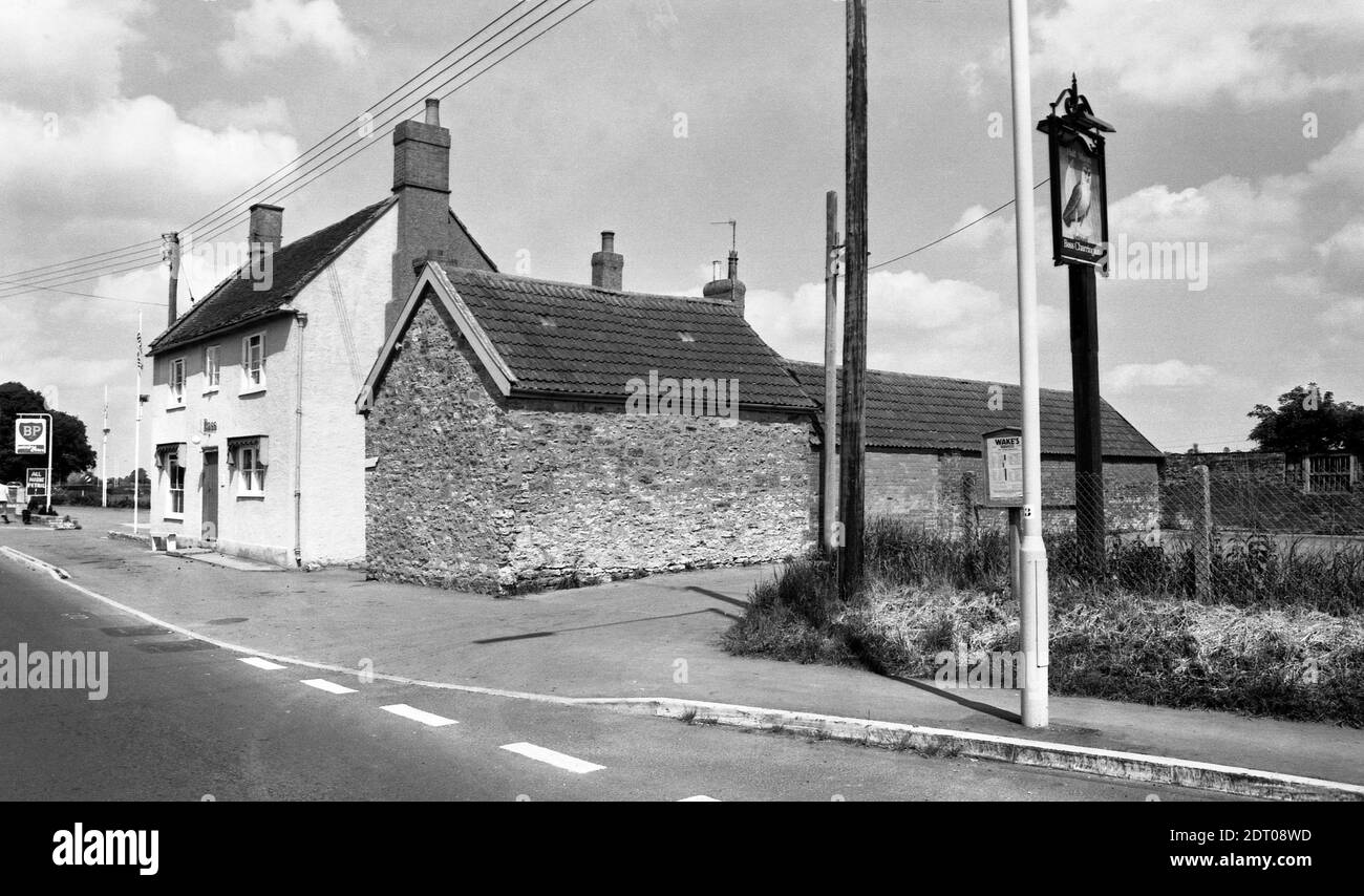 Half Moon in Mudford, near Yeovil in or just before 1975. A front and side elevation. Later photos show an added canopy over the main door. The bus stop advertises times for Wake's Services, the pubs post sign shows an owl in front of a half moon and the BP garage boasts 24 hour petrol (filling station now gone and is a car showroom in 2020). Half Moon Mudford in 1975 number 0348a Stock Photo